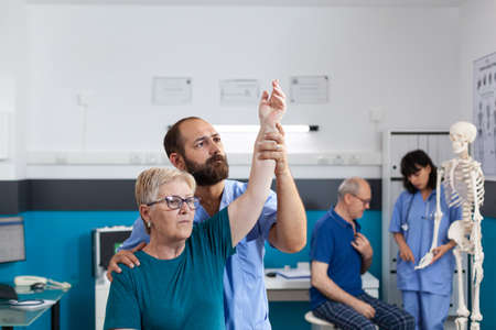 Chiropractor holding arm of old woman to relieve pressure for recovery in osteopathy office. Orthopedic assistant helping senior patient with shoulder muscle pain for healthcare.の写真素材