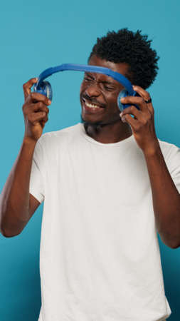 Portrait of joyful person wearing headphones and having fun with song and rhythm. Man listening to music on headset, enjoying audio and doing dance moves. Adult dancing for entertainmentの写真素材
