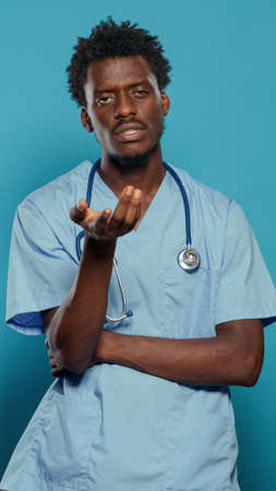 Medical assistant wearing uniform and stethoscope while talking and looking at camera in studio. Man nurse explaining healthcare while standing over isolated background. Health specialistの写真素材