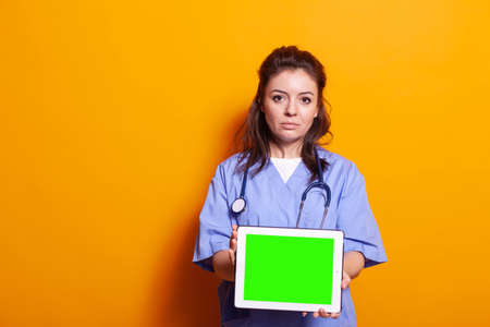 Medical assistant showing digital tablet with horizontal green screen on camera. Woman nurse holding modern gadget with isolated mockup template and background for chroma key on displayの写真素材
