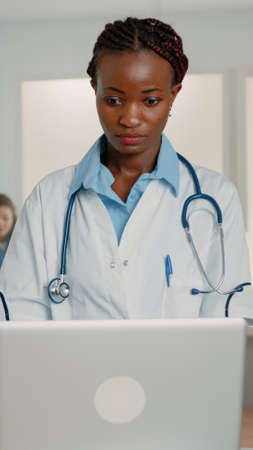 Woman doctor with stethoscope working with modern laptop to cure patient in hospital ward. Medical specialist using gadget to cure disease symptoms and illness with medicine and treatmentの写真素材