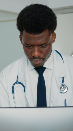 Close up of african american doctor working on computer to treat patient with sickness in hospital ward. General practitioner using monitor to find information about medical treatmentの写真素材
