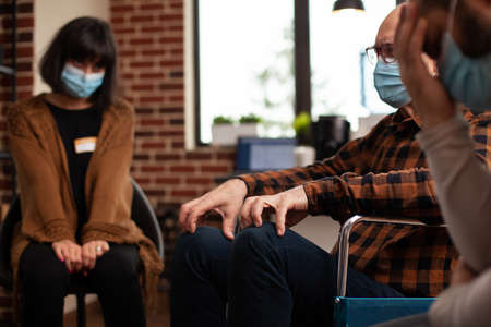 People sitting in circle at aa meeting during virus pandemic. Patients with face masks attending support group therapy session, preparing for discussion and counseling from therapist.の写真素材
