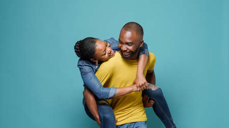 Playful couple having fun with piggy back ride in front of camera. Man carrying woman and enjoying connection together. Joyful people showing affection, having healthy relationship.の写真素材