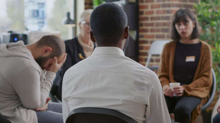 Close up of african american man discussing alcohol addiction at aa therapy session. Adult making confession in front of support group people at rehabilitation program meeting.の写真素材