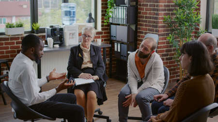 Multi ethnic people having discussion about addiction at aa group therapy in circle. Patients...