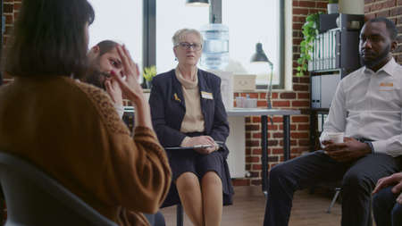 Woman therapist listening to people with addiciton problems at aa group meeting. Psychologist giving support and guidance to patients with mental health problems. Rehab therapyの写真素材