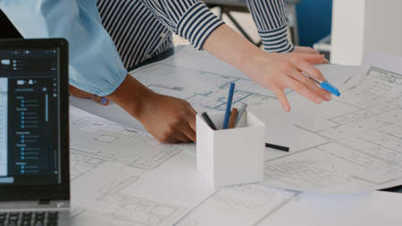Close up of architects doing teamwork to design blueprints plans for building model on table. Team...
