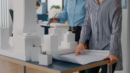 Close up of diverse team of women working on blueprints design in office. Multi ethnic architects using industrial print on table to plan construction layout for architecture project.の写真素材