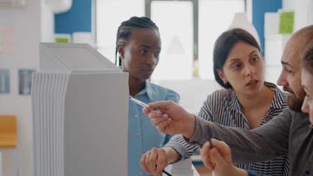 Close up of people working with building model to analyze maquette for construction plan. Colleagues...
