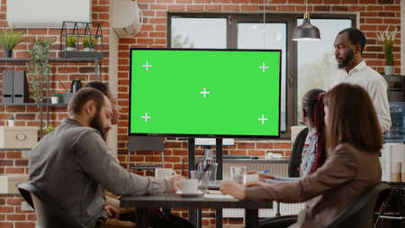 Business man presenting monitor with green screen at meeting with coworkers, looking at mock up...