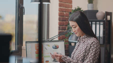 Company employee looking at papers and computer to work on project planning. Woman designing business startegy with documents and charts. Handheld shot of entrepreneur doing analysisの写真素材