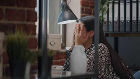 Close up of woman feeling stressed about work deadline in startup office. Entrepreneur working on project planning, feeling burnout and overworked. Busy overwhelmed employee at job.の写真素材