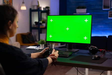 Woman looking at horizontal green screen on monitor, playing video games with controller. Gamer...