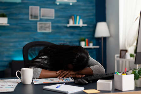 Exhausted employee falling asleep on desk while working from home on papers with data charts. Woman feeling sleepy and doing remote work for design of business project. Tired personの写真素材