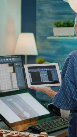 Professional engineer looking at building model on tablet and computer in workplace for...