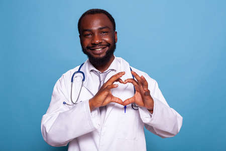 Smiling cardiology doctor making heart shape with hands to show care for health care and patients. Happy medic in lab coat with stethoscope doing the hand gesture for love.の写真素材