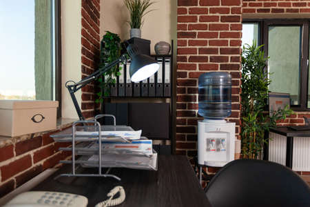Close up of office corner with desk and bookshelf in empty startup space. Nobody at wooden table...