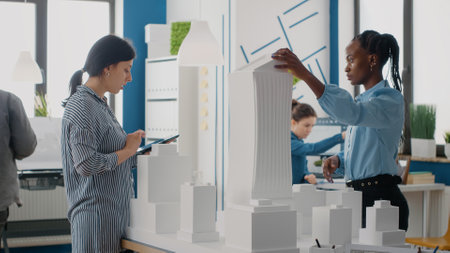 Women using digital tablet to design building model for urban construction in architectural office. Architects working with device and maquette to plan blueprints and architecture project.の写真素材
