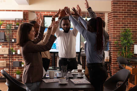 Successful excited diverse businesspeople celebrating winning business partnership rising hands...