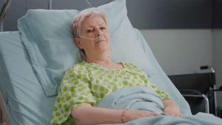 Portrait of senior woman laying in hospital ward bed with nasal oxygen tube and IV drip bag....