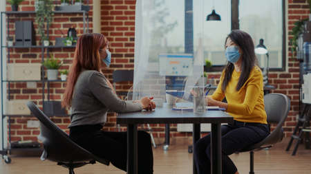 Candidate attending job interview application in business office during covid 19 pandemic. Asian woman talking to hr worker recruiting people for startup employment, having cv resume on desk.の写真素材