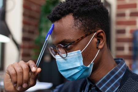 Portrait of african american with glasses wearing face mask and wireless earbuds scratching forehead...