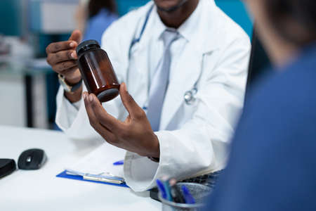 Closeup of african american pediatrician doctor holding pills bottle explaining medication treatment to patient mother during clinical appointment in hospital office. Medicine serviceの写真素材