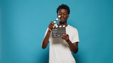 Portrait of man holding clapperboard to cut scenes in movie industry. Cheerful person using chalkboard for film making production and cinematography in studio. Young adult with clap boardの写真素材