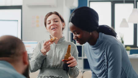 Group of colleagues having fun with drinks after work. Workmates enjoying bottles of beer and pizza while playing at foosball game table for entertainment. Coworkers after hoursの写真素材