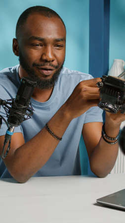 Social media vlogger reviewing tripod head for camera gear on podcast. Influencer holding adjustable tool for stability, recording product review for vlog channel. Man with equipmentの写真素材