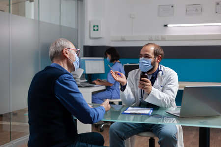 Retired adult receiving bottle of pills from medic at consultation during covid 19 pandemic. Doctor with face mask giving prescription treatment in jar to patient at checkup visit.の写真素材