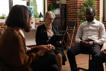 Woman psychologist giving rehab advice to people at aa group therapy session. Therapist meeting with...
