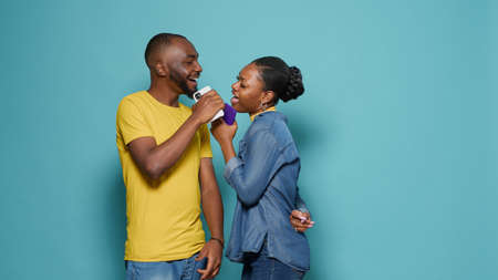 Playful couple singing song and using smartphone as microphone. Man and woman enjoying music and...