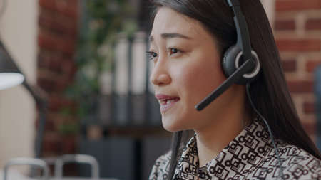 Close up of call center employee with headphones talking on phone call about telemarketing with...