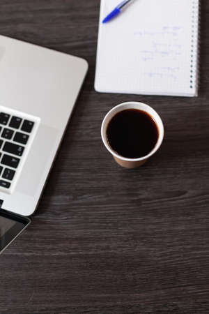 Top view of coffee cup, laptop and notebook on desk. Close up of hot beverage and computer on wooden table, textbook and pen used to take notes at work. Startup business instrumentsの写真素材