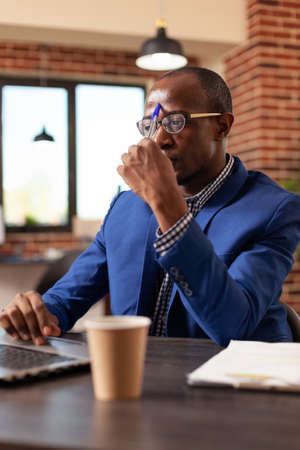 Entrepreneur brainstorming ideas and working on laptop to plan business project in office. Man thinking about solution and invention, planning marketing strategy on computer, feeling thoughful.の写真素材