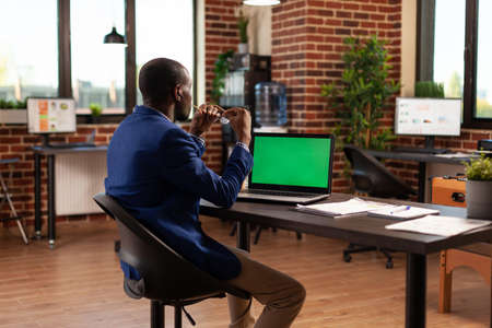 Business man looking at horizontal green screen on laptop to work on project planning. Employee working with chroma key and isolated mockup template on computer display in startup office.の写真素材