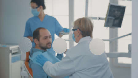 Specialist examining patient with denture problems and caries, preparing for dental surgery at oral care clinic. Dentist doing orthodontic consultation and consulting man in pain.の写真素材