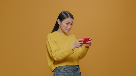 Young adult playing online games on mobile phone, enjoying leisure activity. Asian woman using...
