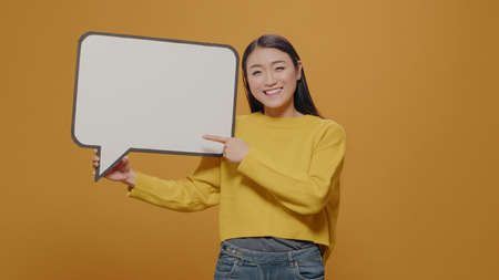Cheerful woman pointing at empty speech bubble in studio, advertising copy space accessory for text...