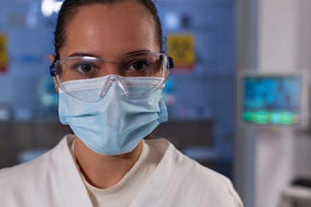 Portrait of scientist researcher wearing protective face mask against covid19 looking into camera. Chemist woman doctor working at biochemical experiment in pharmaceutical hospitalの写真素材