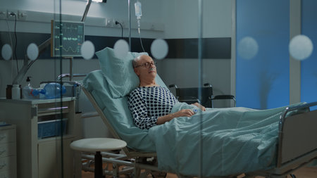 Patient with disease sleeping in hospital ward bed at facility while doctor and nurse passing by room. Medical equipment healing old man with help of nasal oxygen tube and IV drip bagの写真素材