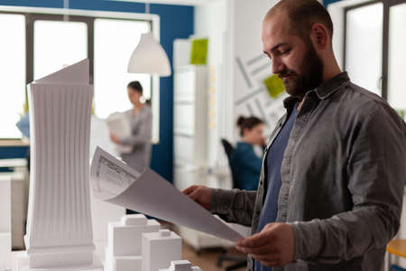 Architect reading blueprint of residential project next to skyscraper maquette in modern...