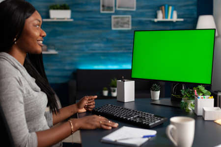Entrepreneur using horizontal green screen on computer doing remote work at home. Business woman looking at monitor display with isolated background and mockup template, working with deviceの写真素材