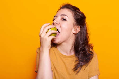Portrait of healthy woman biting green apple in hand on camera. Caucasian person with vegetarian diet advertising organic sweet snack for natural nutrition and fresh meal. Adult bite fruitの写真素材