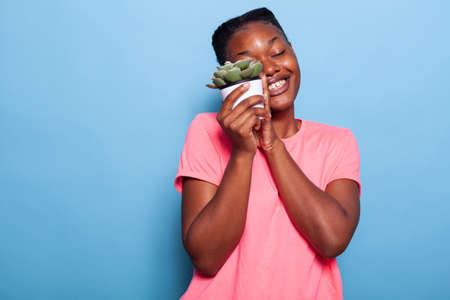 Portrait of african american young woman holding flowerpot smiling at camera standing in studio with...