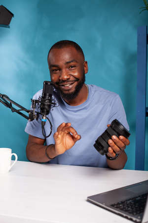 Social media influencer presenting satisfying review of digital camera zoom lens using boom arm microphone. Content creator reviewing photography equipment for online followers in vlogging studio.の写真素材