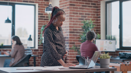 African american woman expecting child and working on business project with documents. Pregnant employee analyzing files to design and plan marketing strategy for development at office.の写真素材