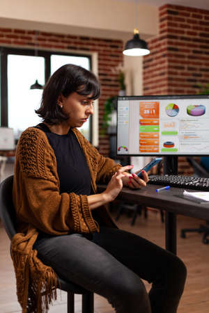 Businesswoman sitting at desk table holding modern phone searching business information working at...